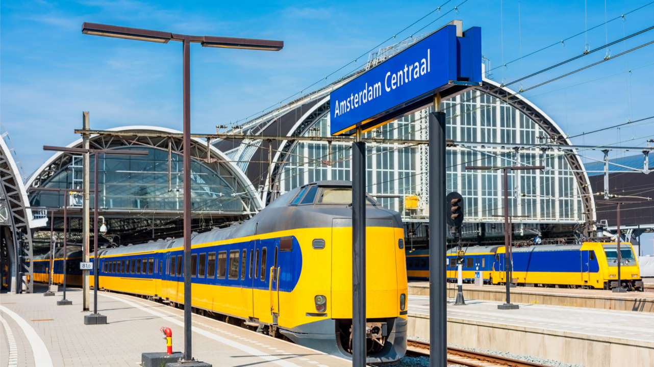 A railway station platform with a steel footbridge as a train approaches.