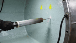Home 49 Coating inspector using high-voltage spark tester for holiday detection on glass flake epoxy tank lining in industrial fabrication shop.